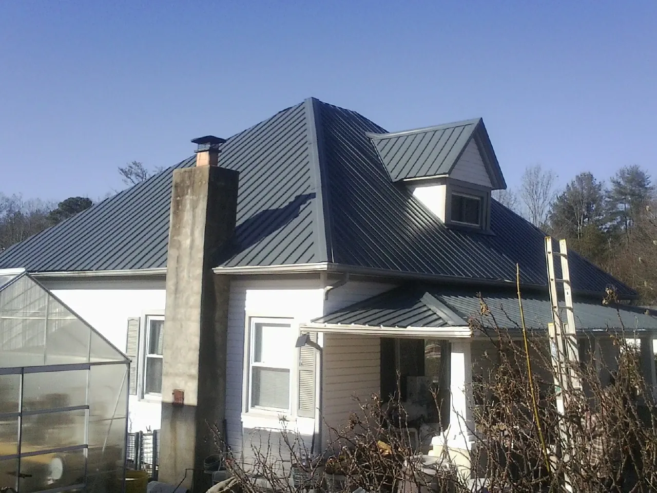 Dark blue standing seam metal roof on a white farmhouse with dormer — Slate & Tile Roof Repair by Roofing Brothers in Piney Point