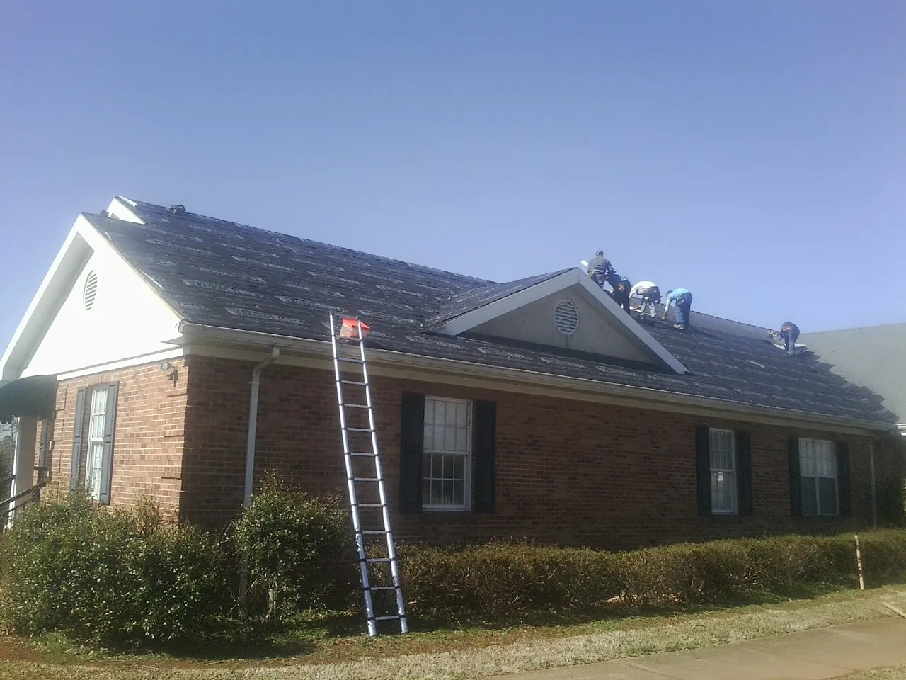 Crew tearing shingles off a brick ranch roof with a ladder set — Metal Roof Repair work by our crew in Piney Point