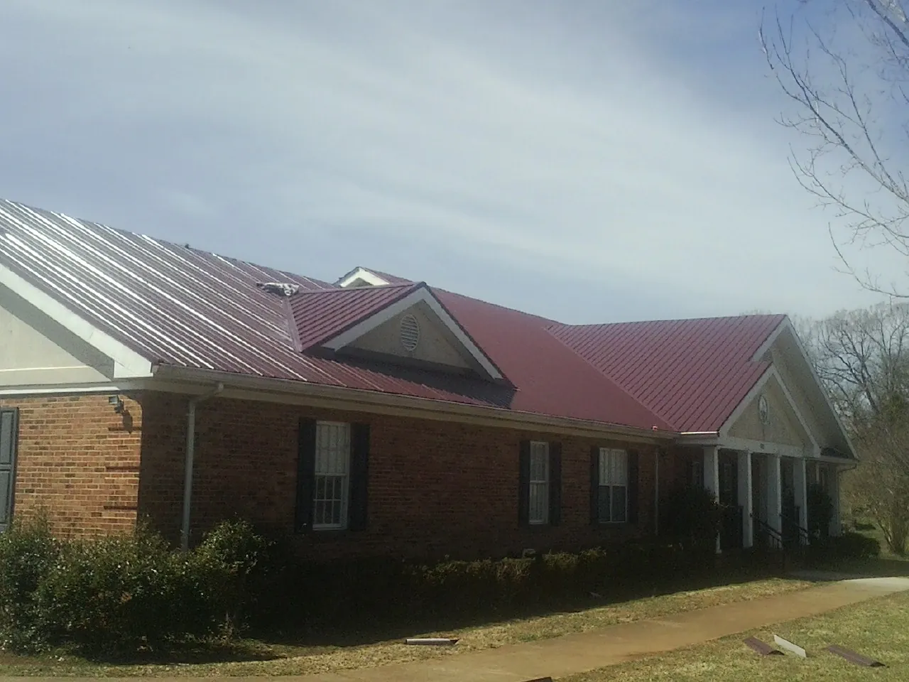 Red metal roof with gabled entries on a long brick building, from a Hail Damage Roof Repair job in Piney Point