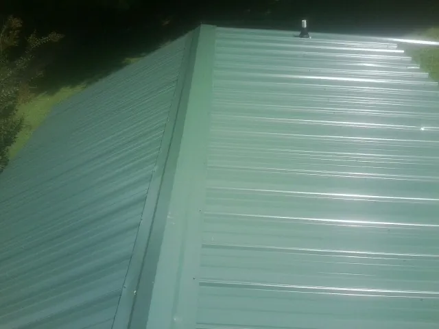 New green metal panels meeting at the ridge of a roof — Flat Roof Repair work by our crew in Piney Point