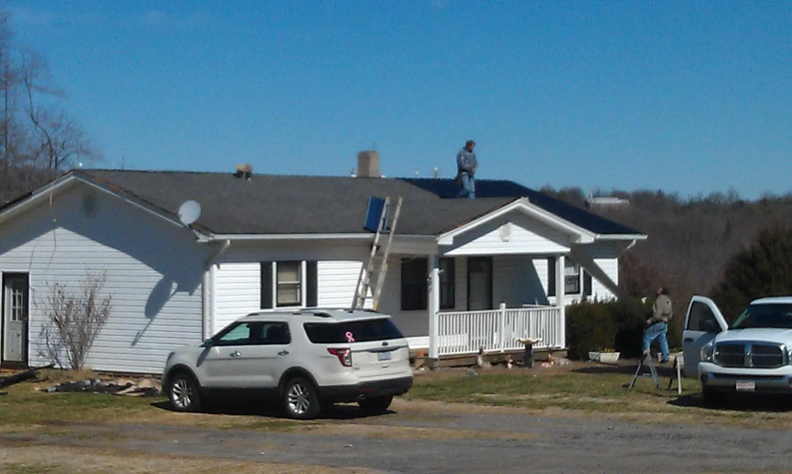 Roofers stripping shingles from a white ranch house roof in Piney Point