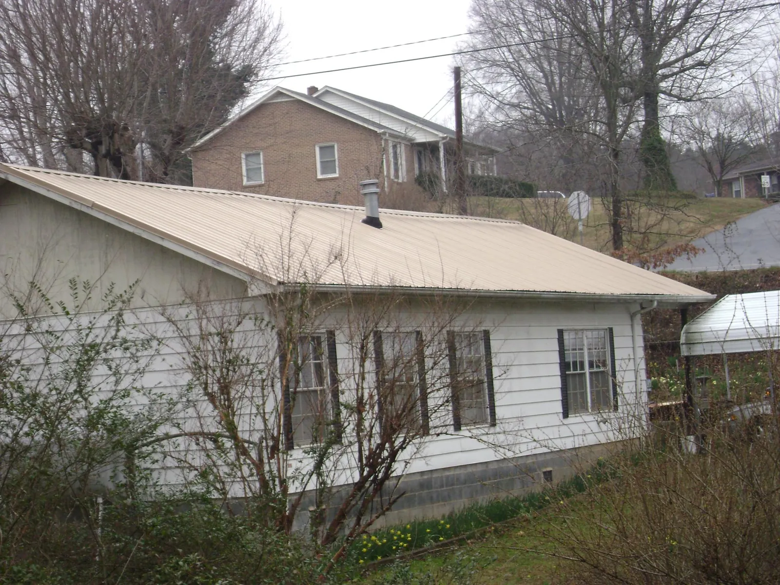 Tan metal roof on a white sided house set into a hillside — Commercial Roofing by Roofing Brothers in Piney Point