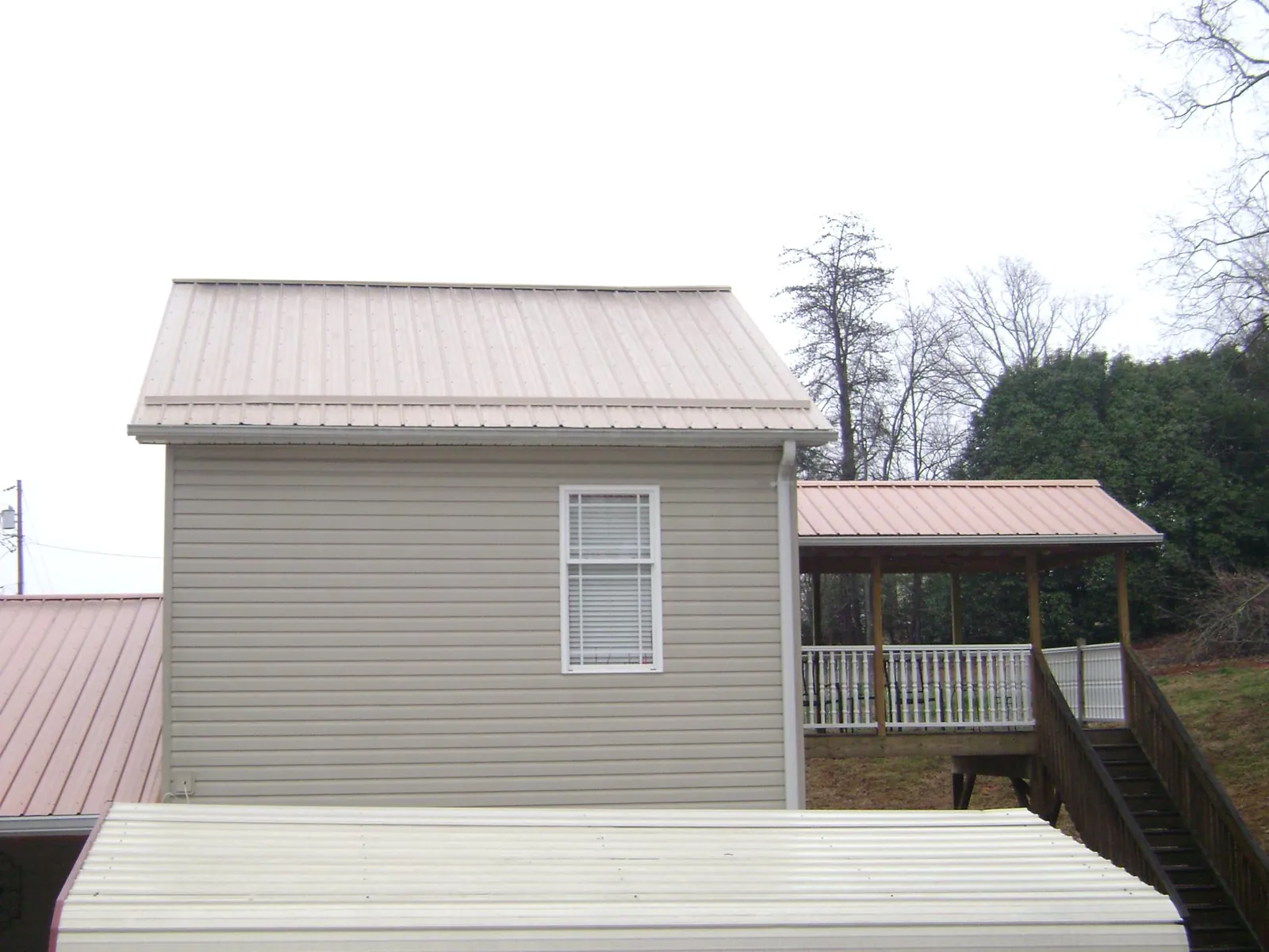 Tan metal roofs on a two story addition and attached porch, from a Roof Replacement job in Piney Point